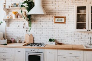 Farmhouse kitchen with white hood fan, painted white brick, butcher block countertops and gas cooktop.